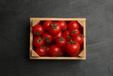 Photo of Fresh ripe cherry tomatoes in wooden crate on black table, top view