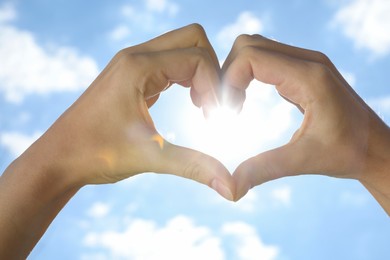 Photo of Woman making heart with hands against blue sky, closeup