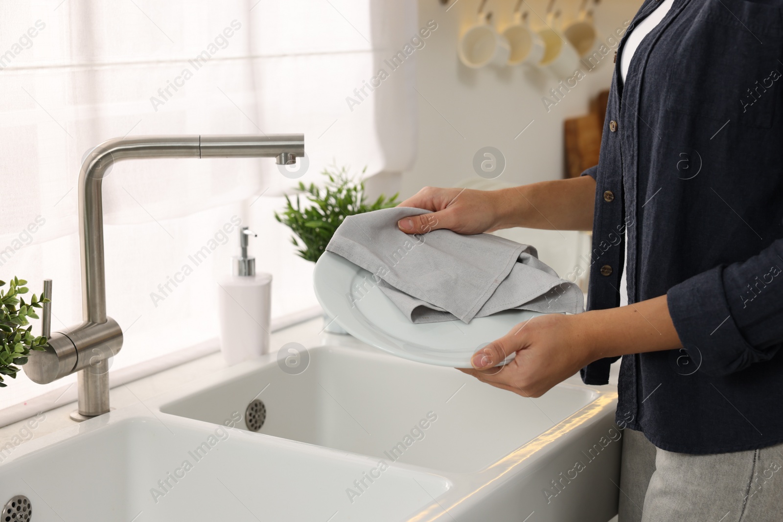 Photo of Woman wiping plate with towel in kitchen, closeup