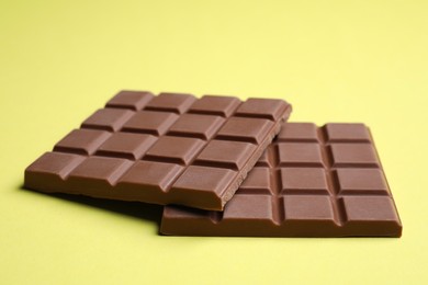 Photo of Pieces of tasty milk chocolate bar on pale yellow background