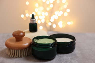 Natural scrub and other body care products on grey table against blurred lights