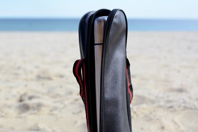 Photo of Metallic thermos in black stylish case on sandy beach