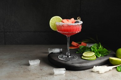 Photo of Cocktail glass of delicious fresh watermelon juice, lime, mint and ice on grey table