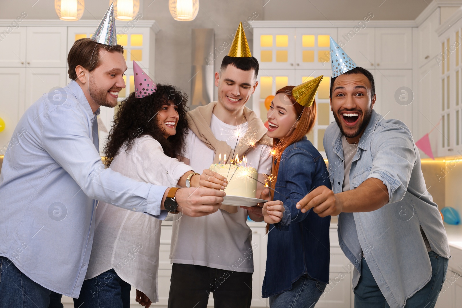 Photo of Happy friends with tasty cake and sparklers celebrating birthday in kitchen