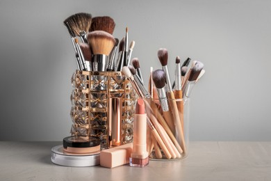 Photo of Set of professional brushes and makeup products on table against grey background