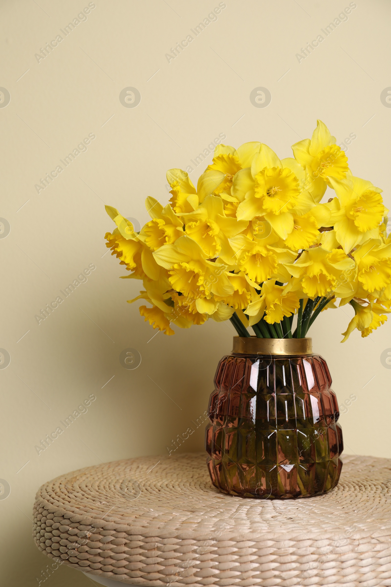 Photo of Beautiful daffodils in vase on wicker table near light wall