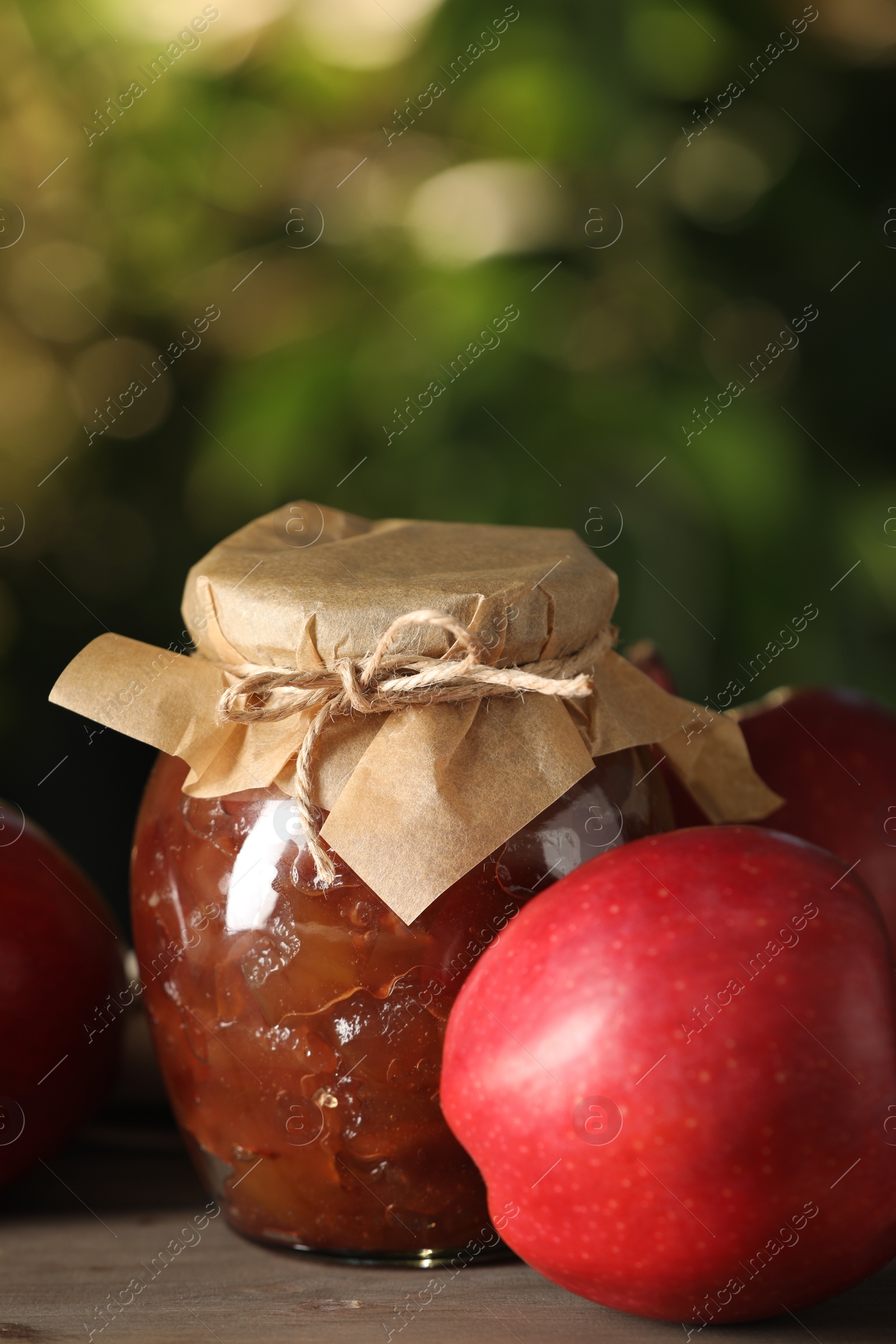 Photo of Glass jar with delicious apple jam and fresh fruits on wooden table against blurred background, closeup. Space for text