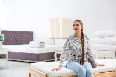 Photo of Young woman testing mattress in furniture store. Space for text