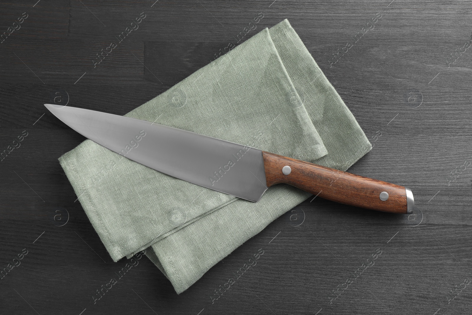 Photo of One sharp knife and napkin on black wooden table, top view