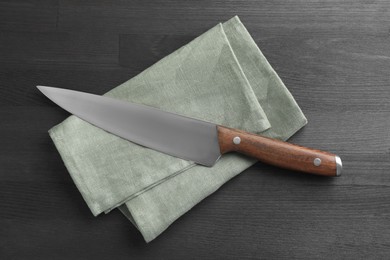 Photo of One sharp knife and napkin on black wooden table, top view