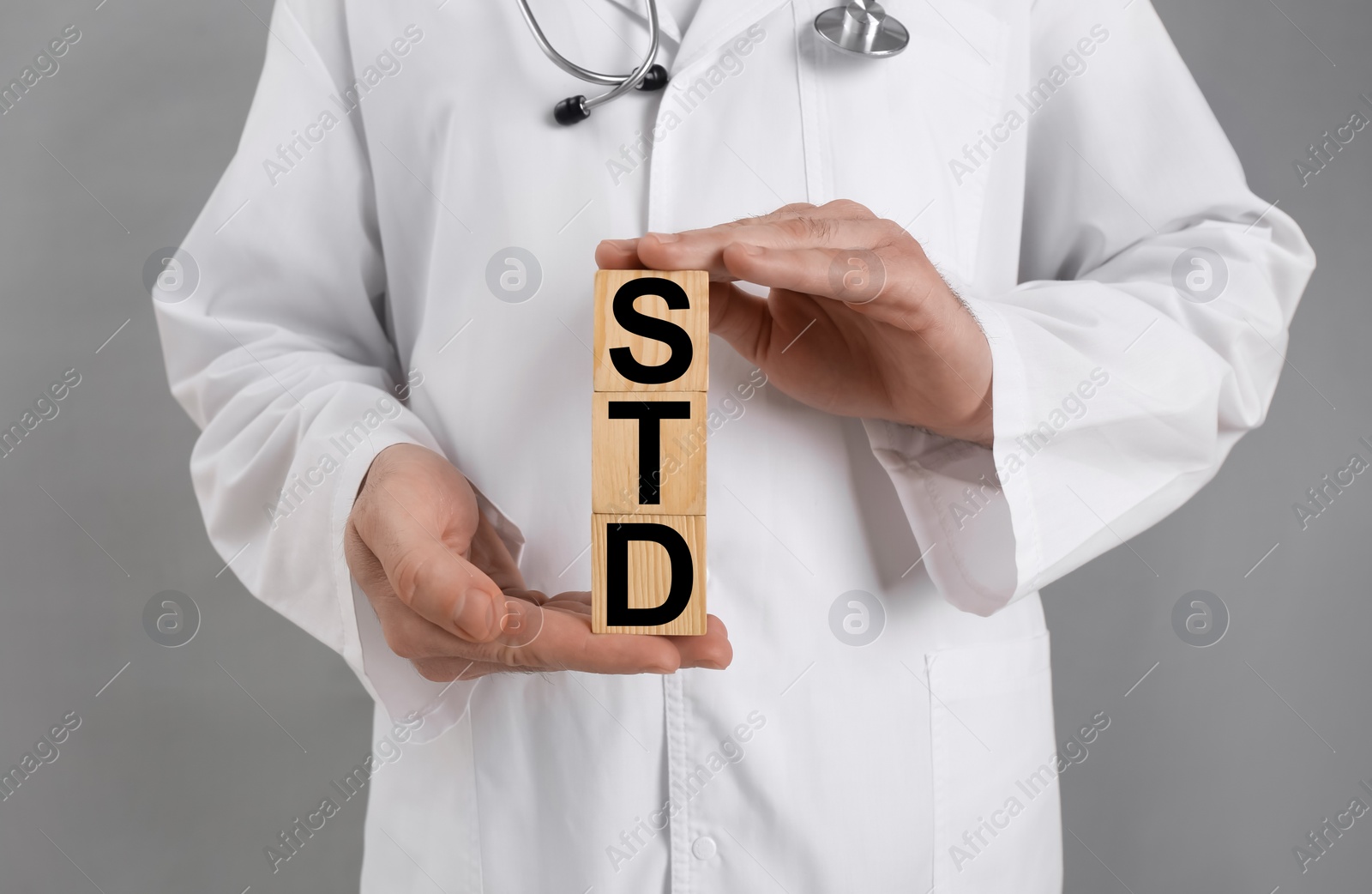 Photo of Doctor holding wooden cubes with abbreviation STD on grey background, closeup