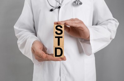 Photo of Doctor holding wooden cubes with abbreviation STD on grey background, closeup