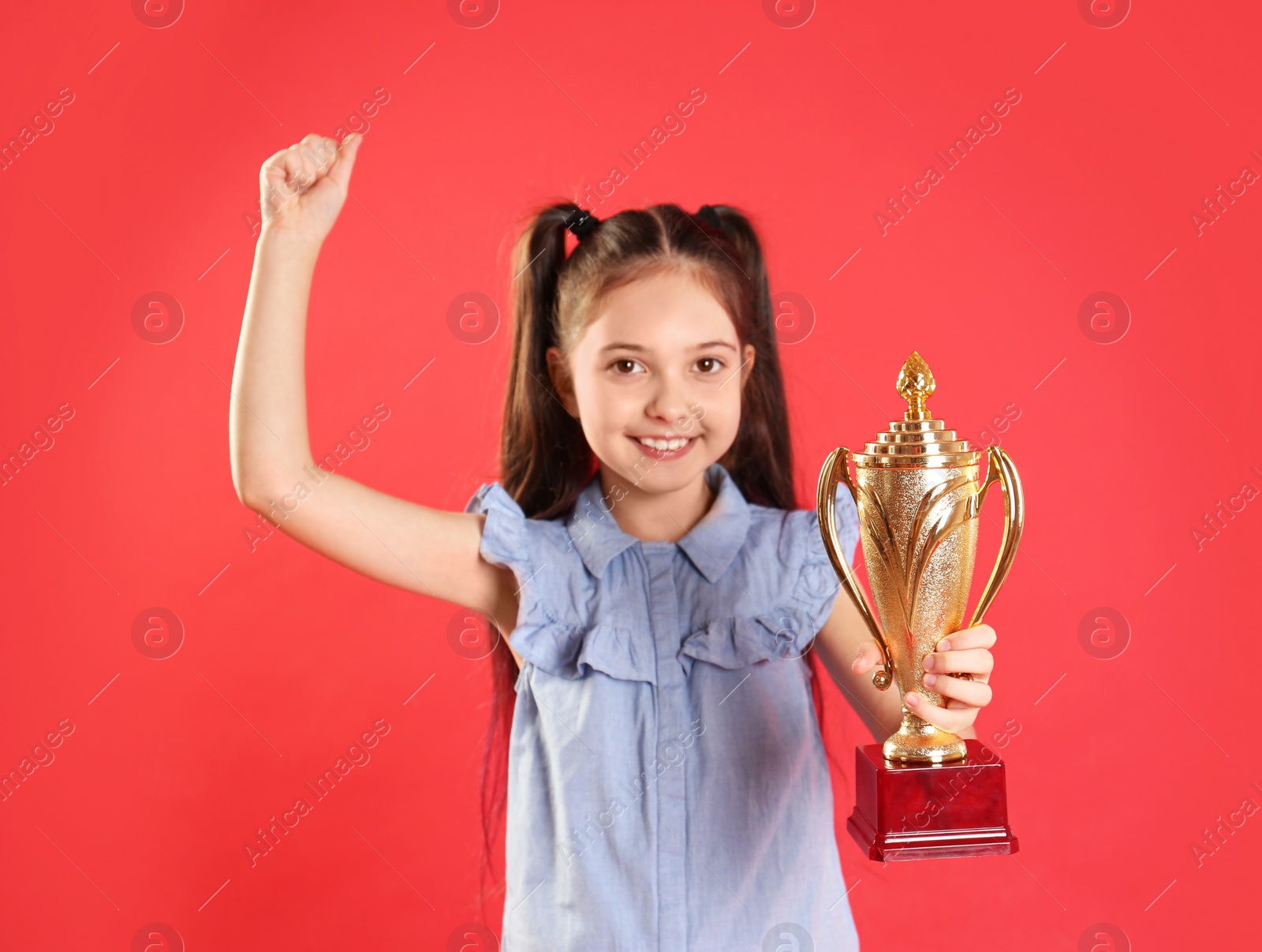 Photo of Happy girl with golden winning cup on red background