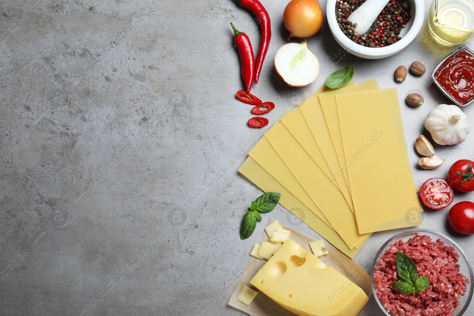 Photo of Fresh lasagna ingredients on grey table, flat lay. Space for text