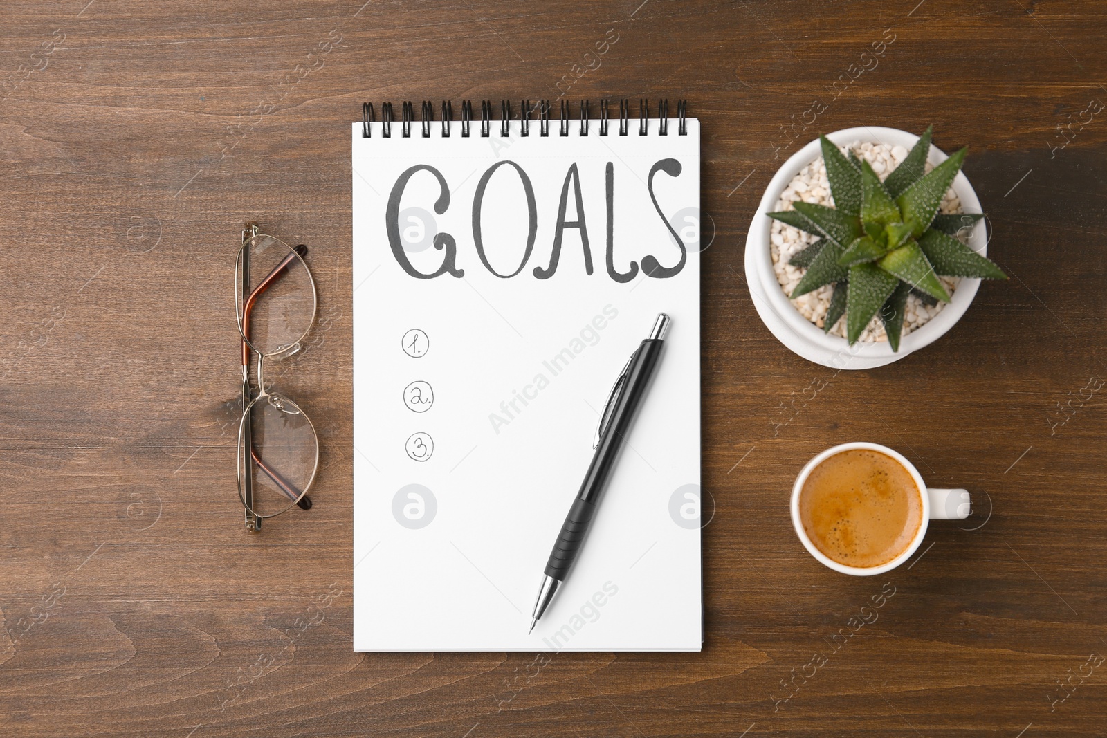 Photo of Notebook with empty list of goals, houseplant, glasses, pen and cup of coffee on wooden table, flat lay