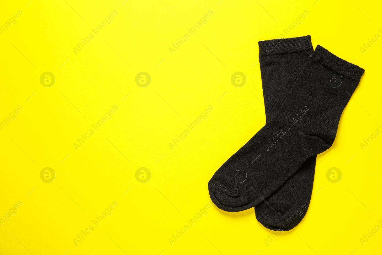 Photo of Pair of black socks on yellow background, flat lay. Space for text