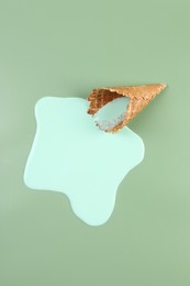 Photo of Melted ice cream and wafer cone on green background, top view