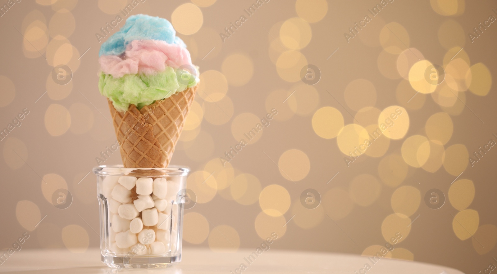 Photo of Sweet cotton candy in waffle cone on table against blurred lights, closeup. Space for text