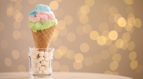 Photo of Sweet cotton candy in waffle cone on table against blurred lights, closeup. Space for text