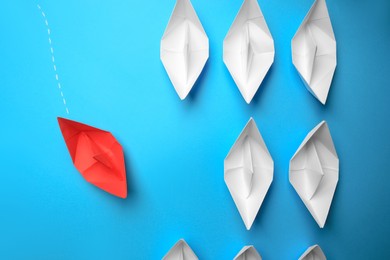 Photo of Red paper boat floating to others on light blue background, flat lay. Uniqueness concept