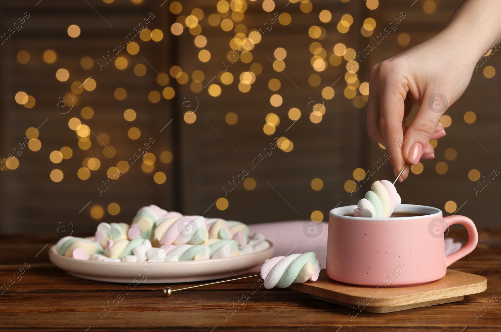 Photo of Woman dipping marshmallow into cup of delicious hot chocolate at wooden table, closeup