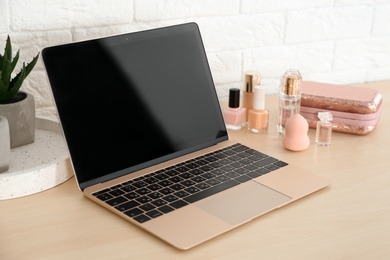 Photo of Stylish workplace with modern laptop and cosmetic products on table near brick wall. Beauty blogger