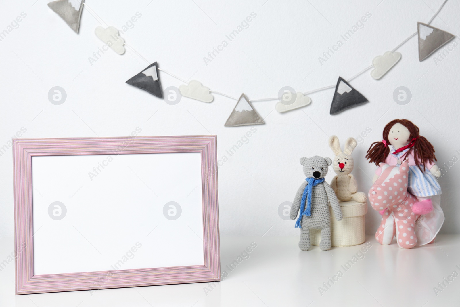 Photo of Soft toys and photo frame on table against white background, space for text. Child room interior