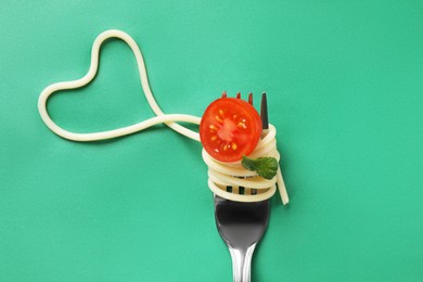 Photo of Heart made of tasty spaghetti, fork, tomato and basil on green background, top view