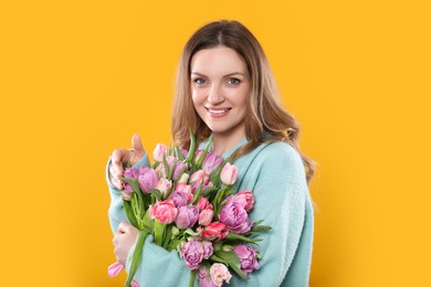 Happy young woman with bouquet of beautiful tulips on yellow background