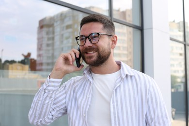 Handsome bearded man in glasses talking on phone outdoors