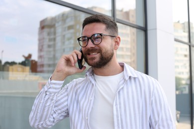 Photo of Handsome bearded man in glasses talking on phone outdoors