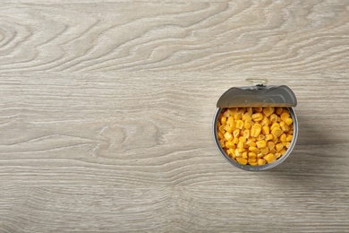 Photo of Open tin can of corn kernels on wooden background, top view. Space for text