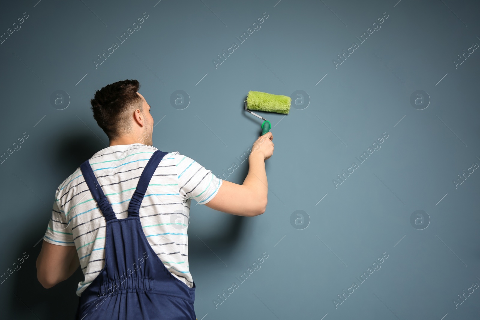 Photo of Young male decorator with paint roller near color wall