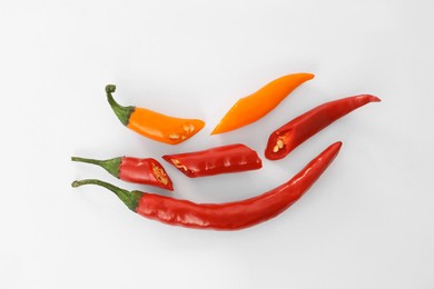 Photo of Whole and cut different hot chili peppers on white background, flat lay