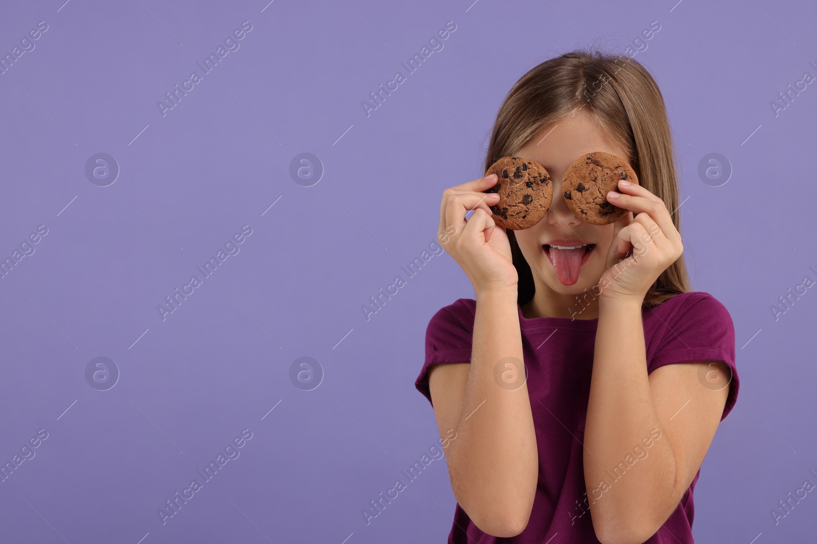 Photo of Girl covering eyes with chocolate chip cookies and showing tongue on purple background. Space for text