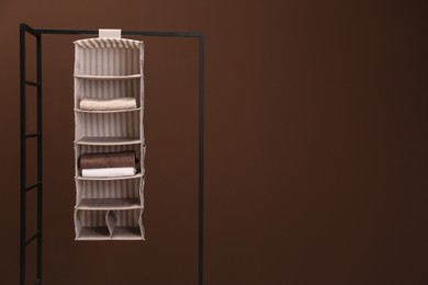 Foldable organizer on rack against brown background. Space for text
