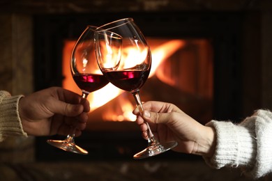 Photo of Couple clinking glasses of wine near fireplace at home, closeup