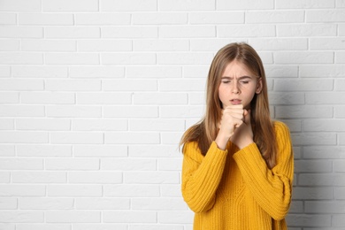 Photo of Teenage girl suffering from cough near brick wall. Space for text