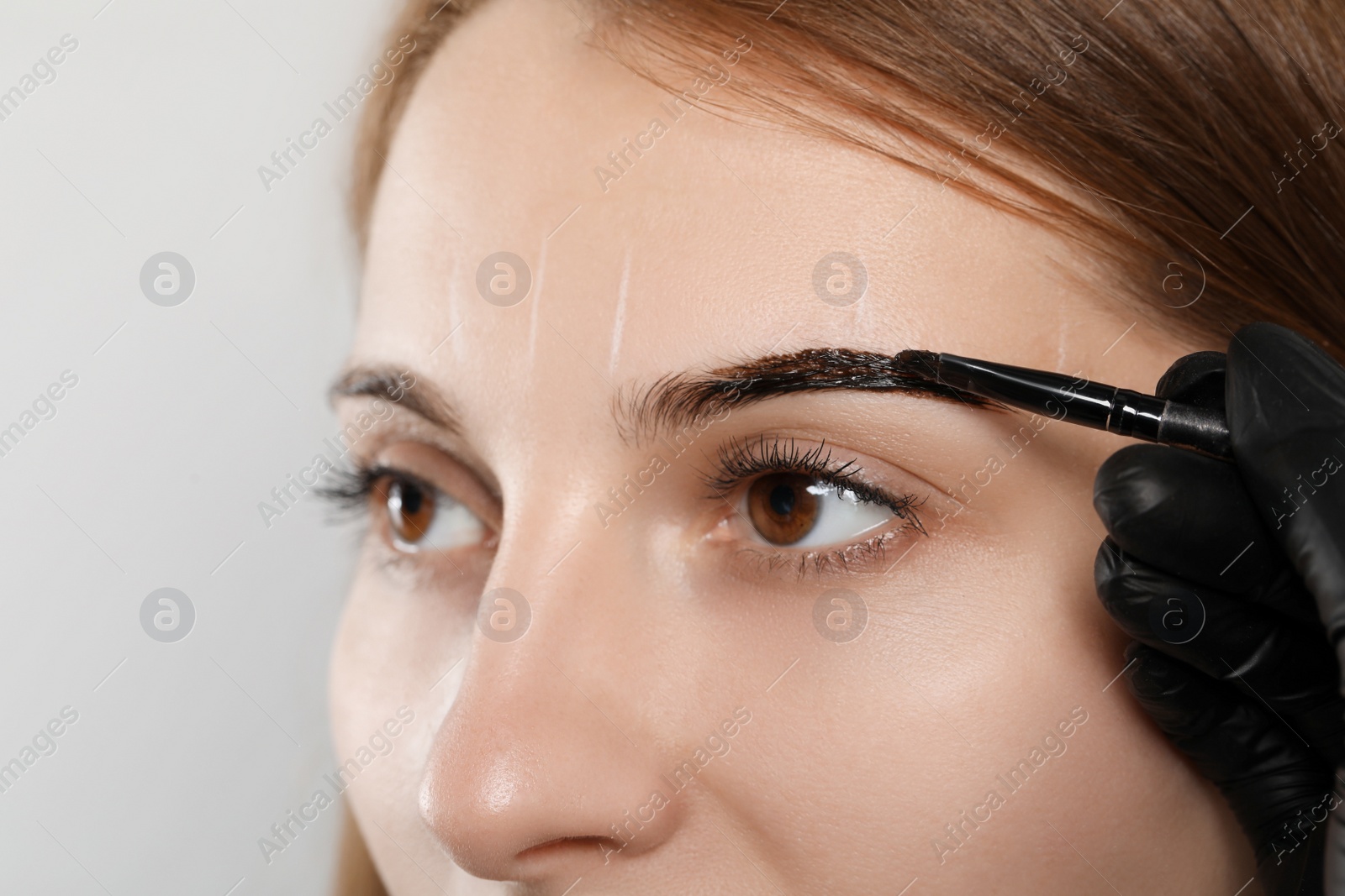 Photo of Beautician applying tint during eyebrows correction procedure on grey background, closeup