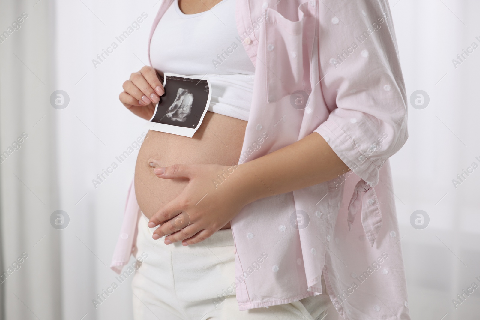 Photo of Pregnant woman with ultrasound picture of baby near window indoors, closeup