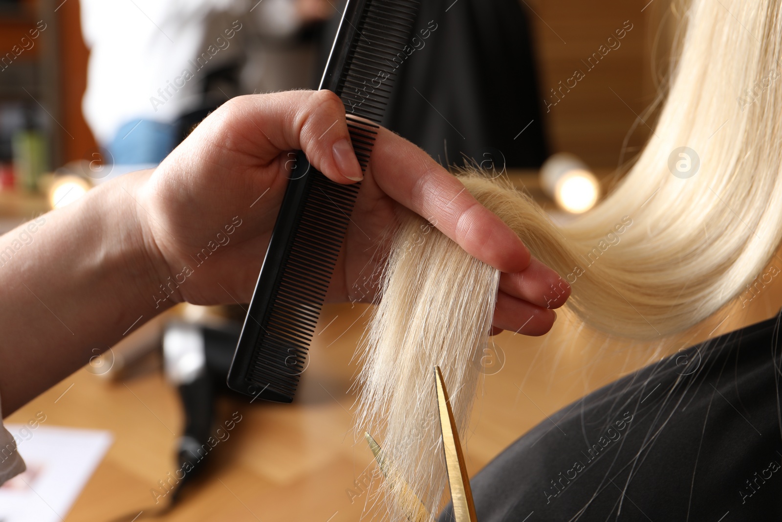 Photo of Hairdresser cutting client's hair with scissors in salon, closeup