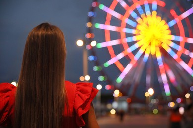 Photo of Beautiful young woman against glowing Ferris wheel in amusement park, back view. Space for text