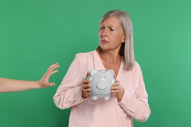 Scammer taking piggy bank from woman on green background. Be careful - fraud