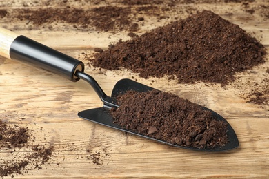 Photo of Metal gardening trowel with soil on wooden table