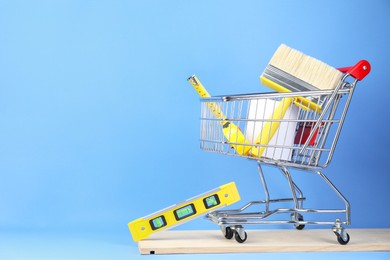 Photo of Small shopping cart with paint and renovation equipment on light blue background
