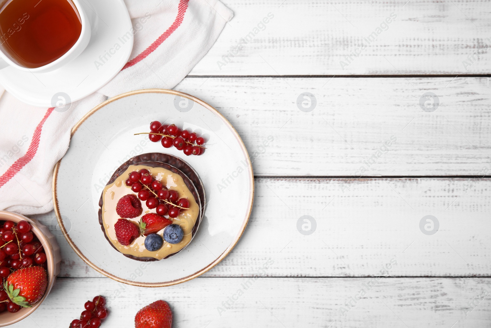Photo of Crunchy rice cakes with peanut butter and sweet berries served on white wooden table, flat lay. Space for text