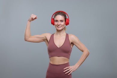 Photo of Sportswoman with headphones showing muscles on grey background