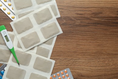 Mustard plasters, pills and thermometer on wooden table, flat lay. Space for text