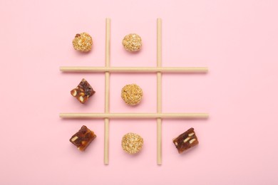 Photo of Tic tac toe game made with sweets on pink background, top view