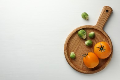 Photo of Cutting board with Brussels sprouts and tomatoes on white wooden table, top view. Space for text